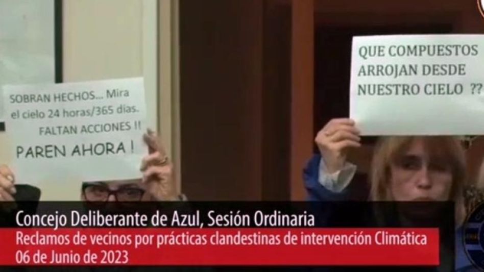 Vecinos en la sesión del Concejo con carteles sobre los chemtrails. (Captura de video)